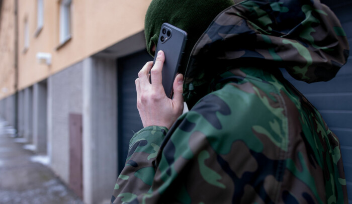 En man går utmed en fasad med ryggen vänd mot kameran, han pratar i mobiltelefon, man ser inte hans ansikte.